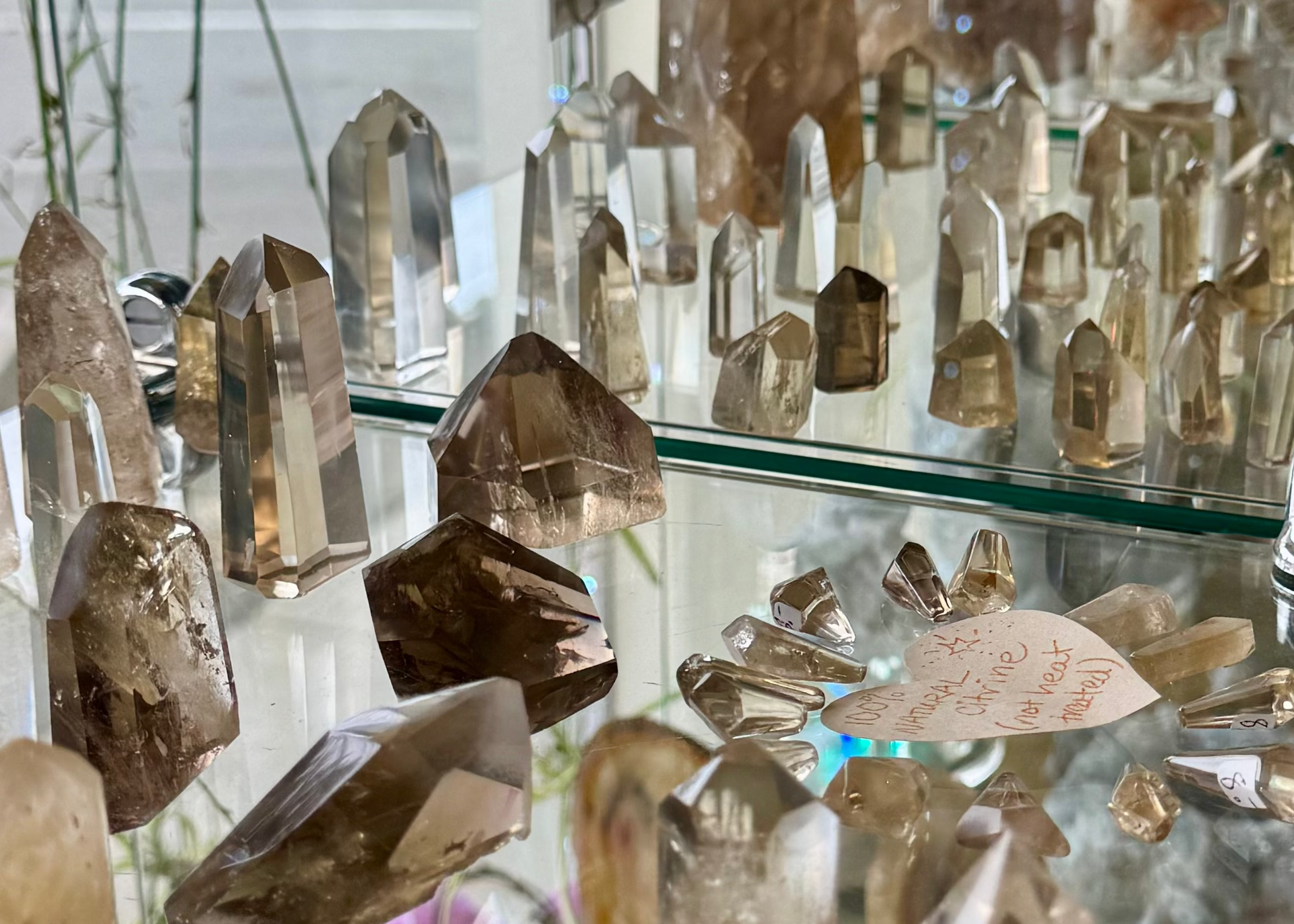 A display of various raw and polished crystals and quartz points arranged on glass shelves, including smoky Citrine, Vibrant to pale yellow Citrine points.